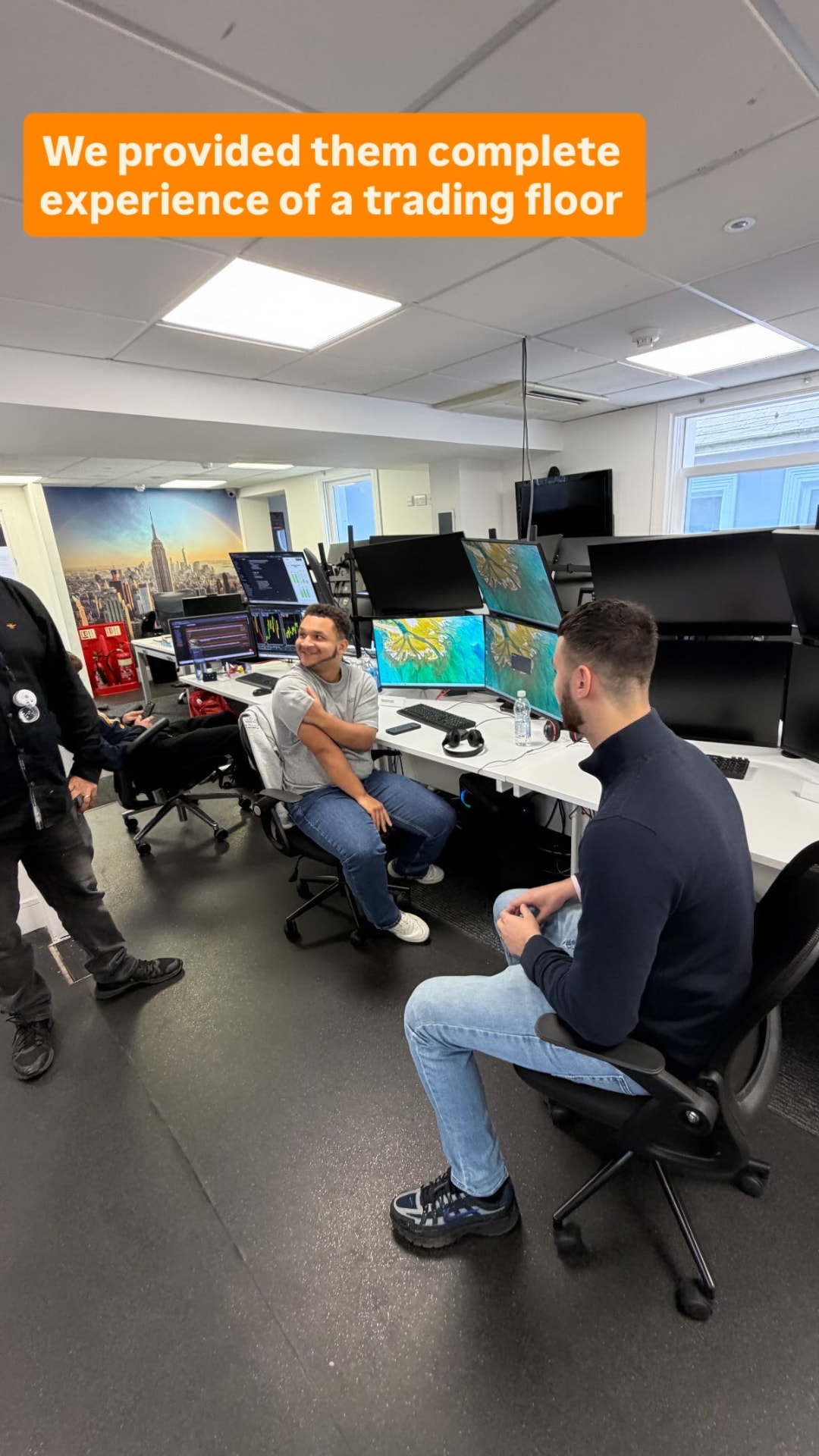 Students sitting at multi-monitor trading desks with mentors